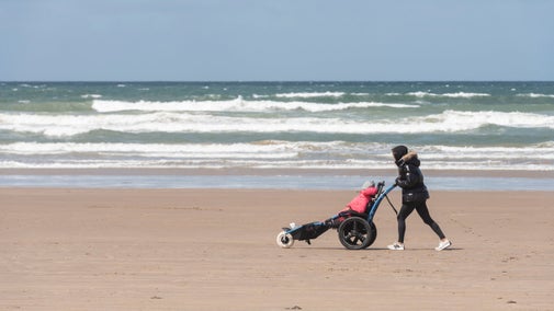 A photograph of a wheelchair user being pushed along Portstewart Strand.